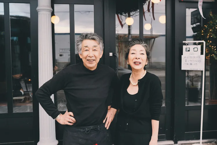 Smiling small-business owners standing outside their café